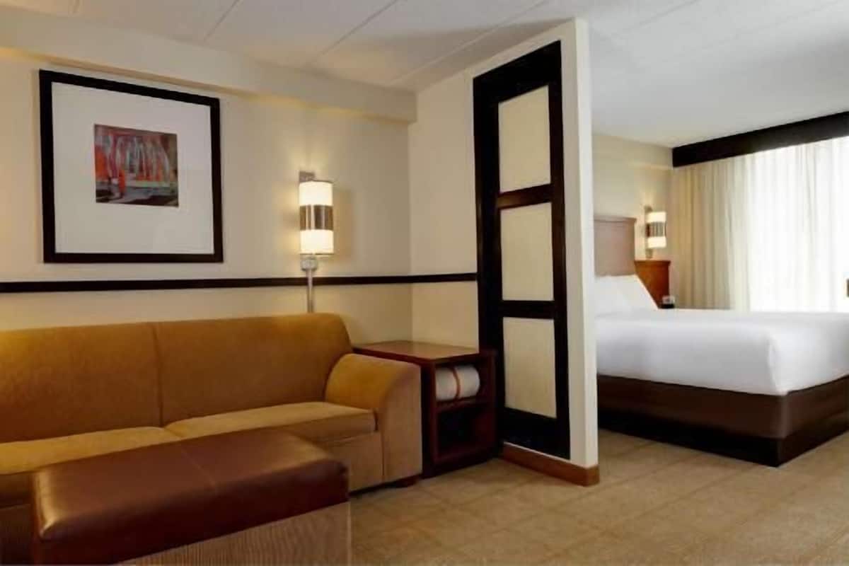 Una habitación de hotel con sofá, cama, mesita de noche, lámpara y un cuadro en la pared.