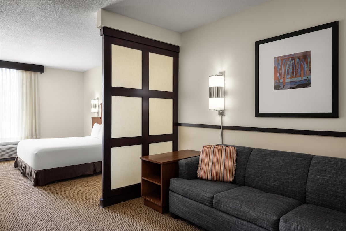 Una habitación de hotel con una cama, un sofá, una mesita pequeña, una lámpara de pared y un cuadro enmarcado.