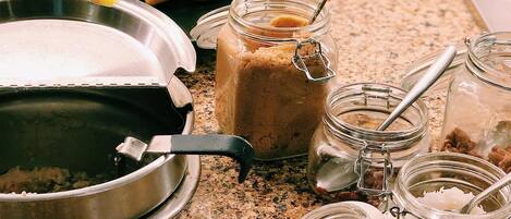 Un comptoir de cuisine avec une casserole en métal, un pot de beurre de cacahuète, un pot de sucre, un pot de sel et une grappe de bananes.