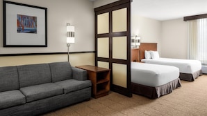 A hotel room with a gray sofa, two single beds, a wooden nightstand, a framed picture on the wall, and a patterned carpet. - Hyatt Place Memphis/Germantown (Memphis)
