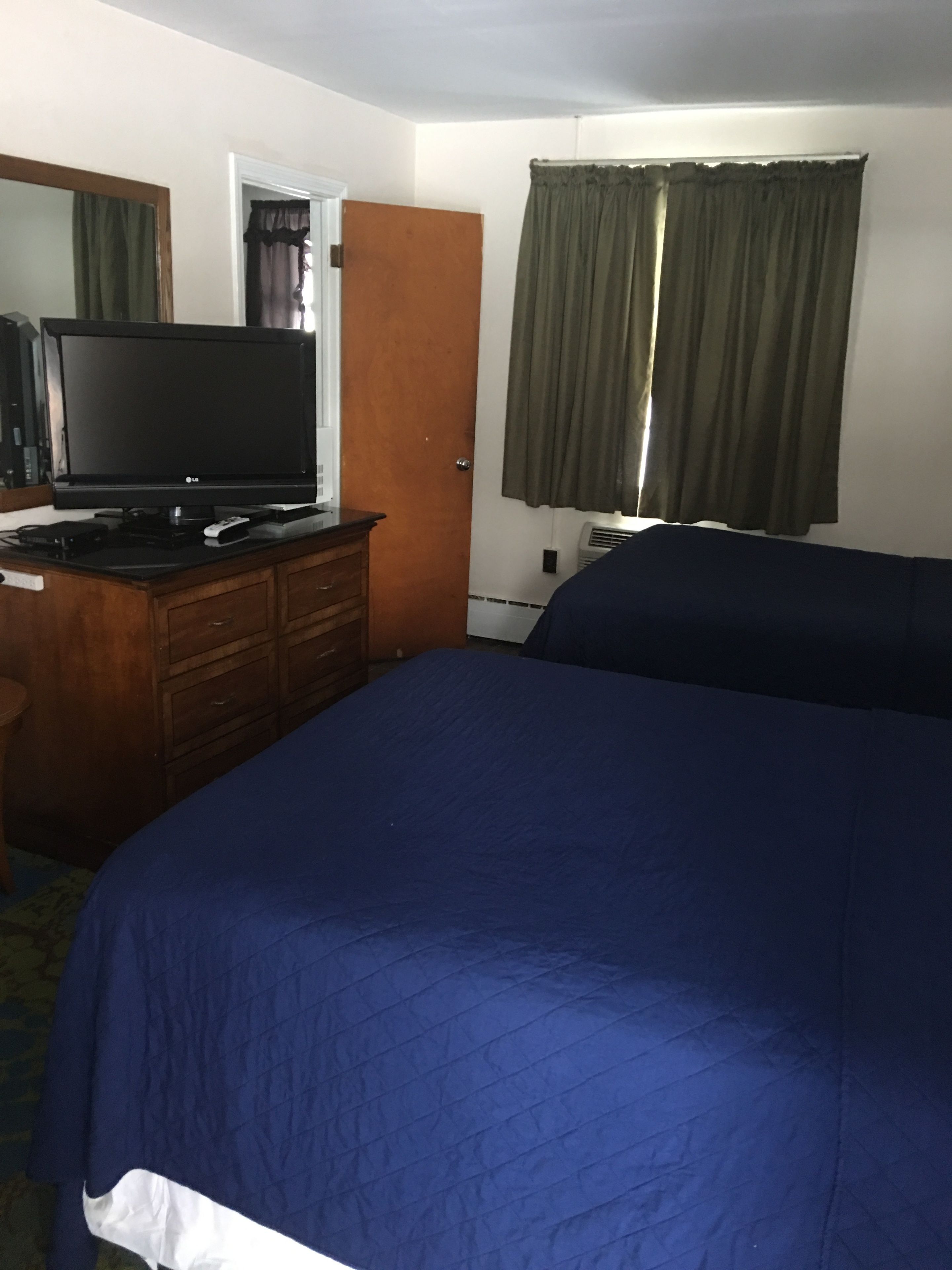 A hotel room with a large bed, a wooden dresser, a flat-screen TV, and a window with curtains.
