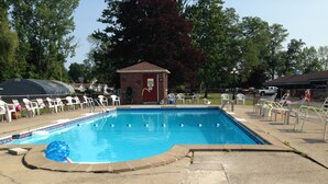A rectangular swimming pool with a tiled edge, surrounded by white lounge chairs and a brick structure labeled "PHYSICAL STORAGE AREA" in the background. - Anchor Motel (Niagara Falls)