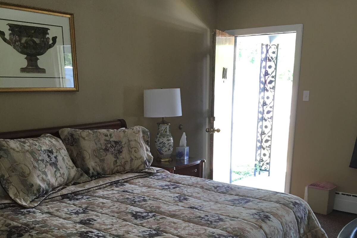 A neatly made bed with floral bedding, a bedside table with a lamp, and a framed picture on the wall.