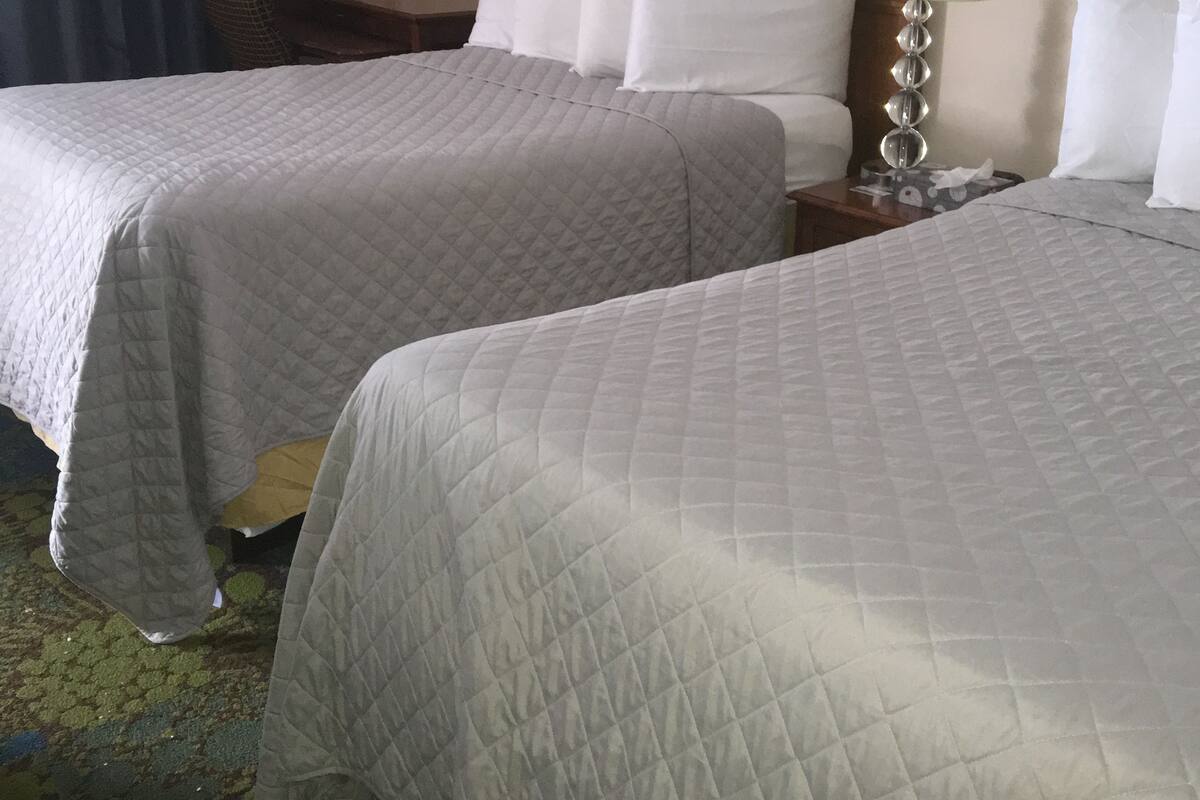 A hotel room with two beds, a desk, a chair, a lamp, and a painting on the wall.