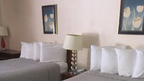 A hotel room with two beds, a nightstand with a lamp, and two framed pictures on the wall. - Anchor Motel (Niagara Falls)