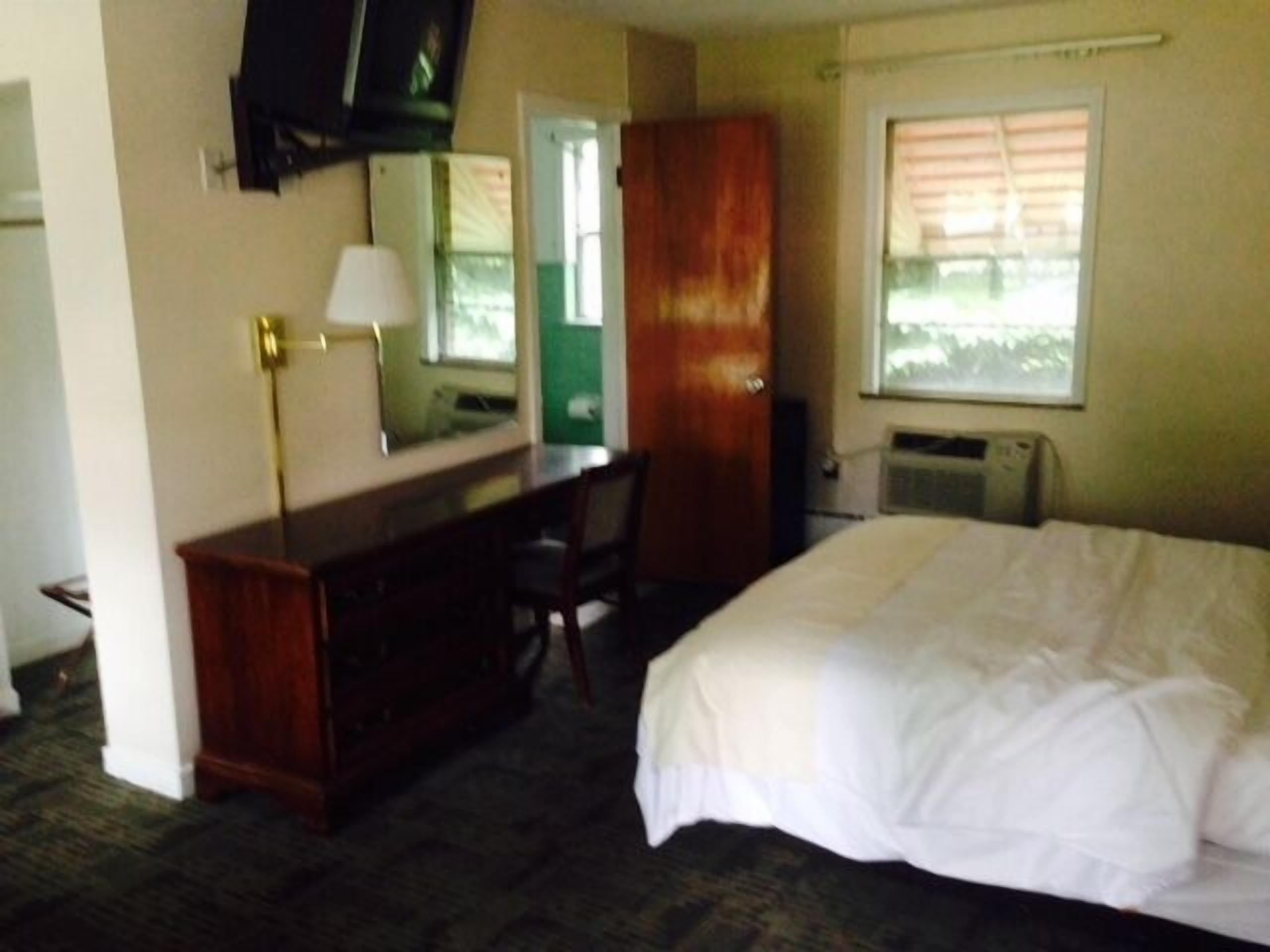 Ein Hotelzimmer mit einem Bett, einem Schreibtisch, einem Stuhl, einem Fernseher und einem Fenster mit Jalousien.