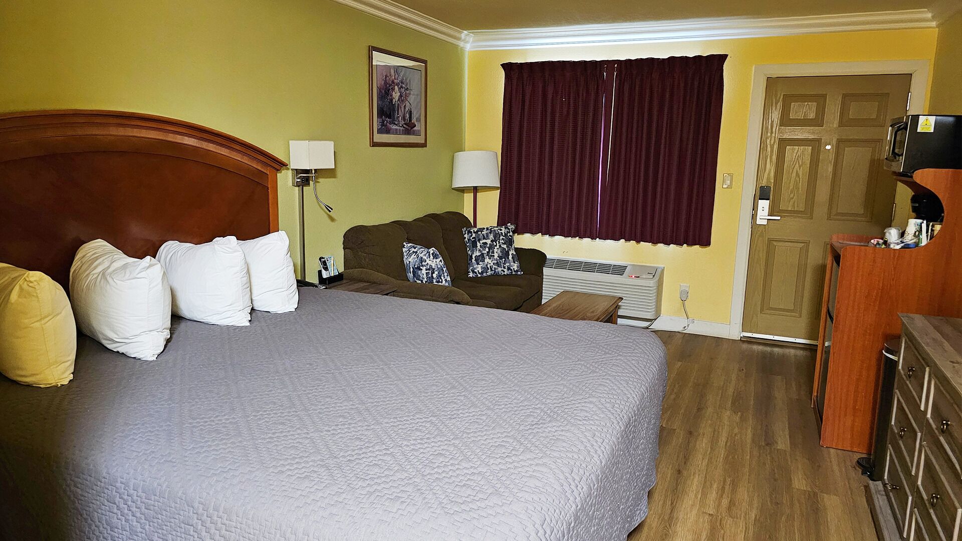 A hotel room with a large bed, a brown sofa, two lamps, a heater, and a wooden dresser.