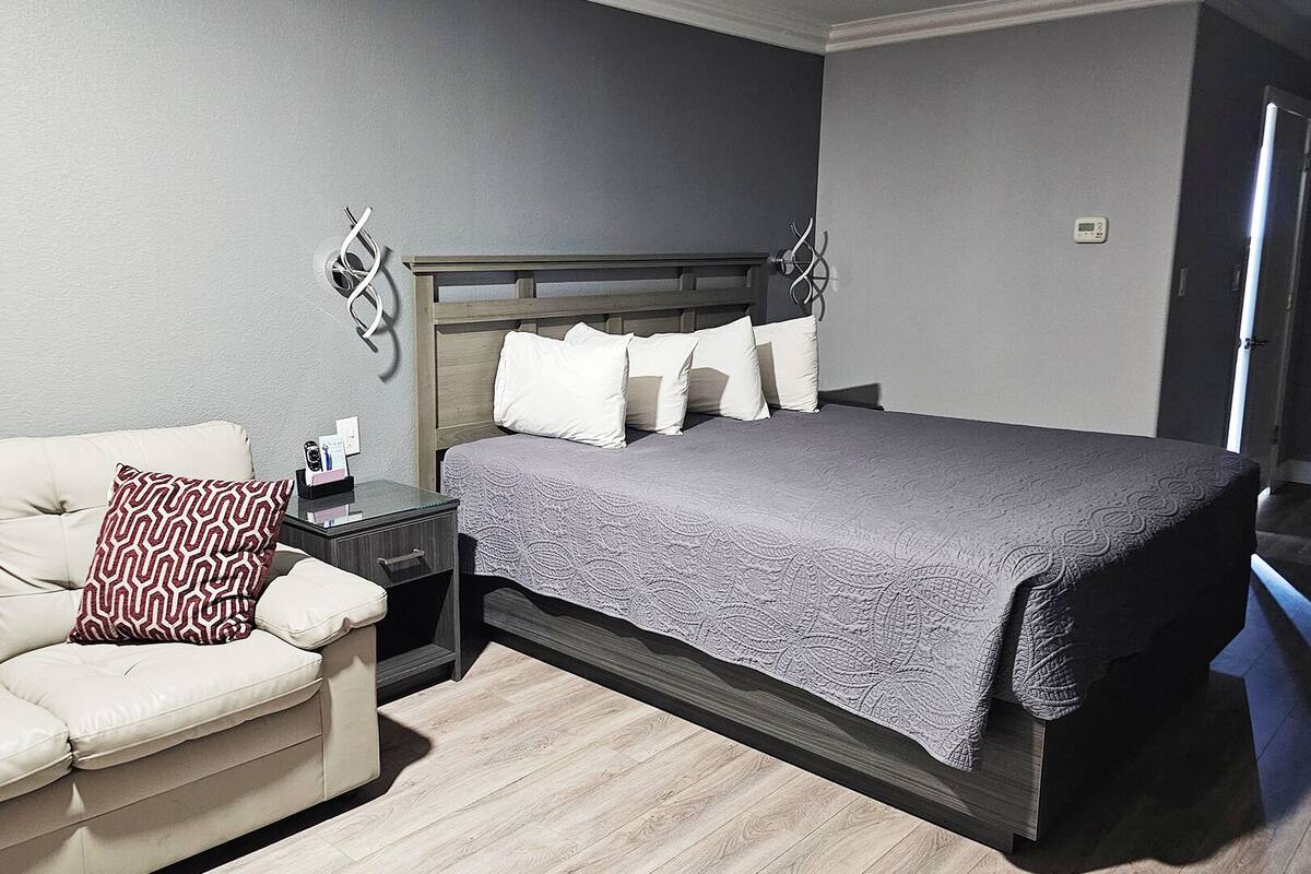 A bedroom with a bed, a sofa, a nightstand, and a wall-mounted light fixture.