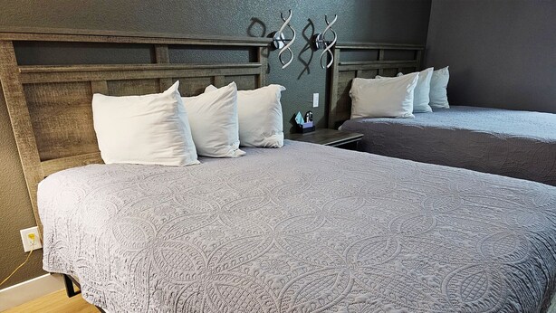 A hotel room with two beds, a wooden headboard, and a wall-mounted light fixture. - Magnuson Hotel Blythe (Blythe)