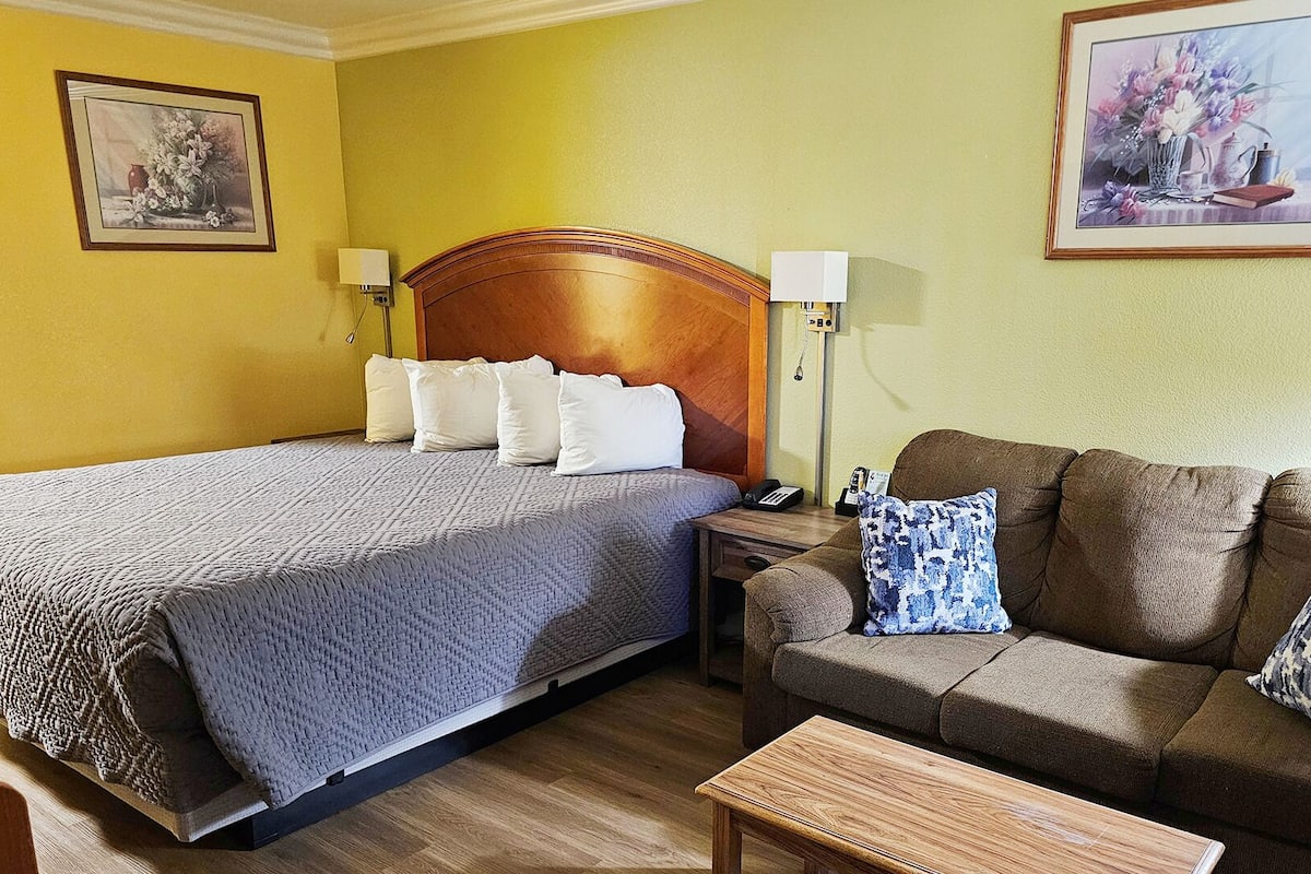 A hotel room with a bed, a sofa, a nightstand, and two wall-mounted lamps.