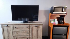 A TV on a wooden cabinet, a microwave on a shelf, and a coffee maker. - Magnuson Hotel Blythe (Blythe)