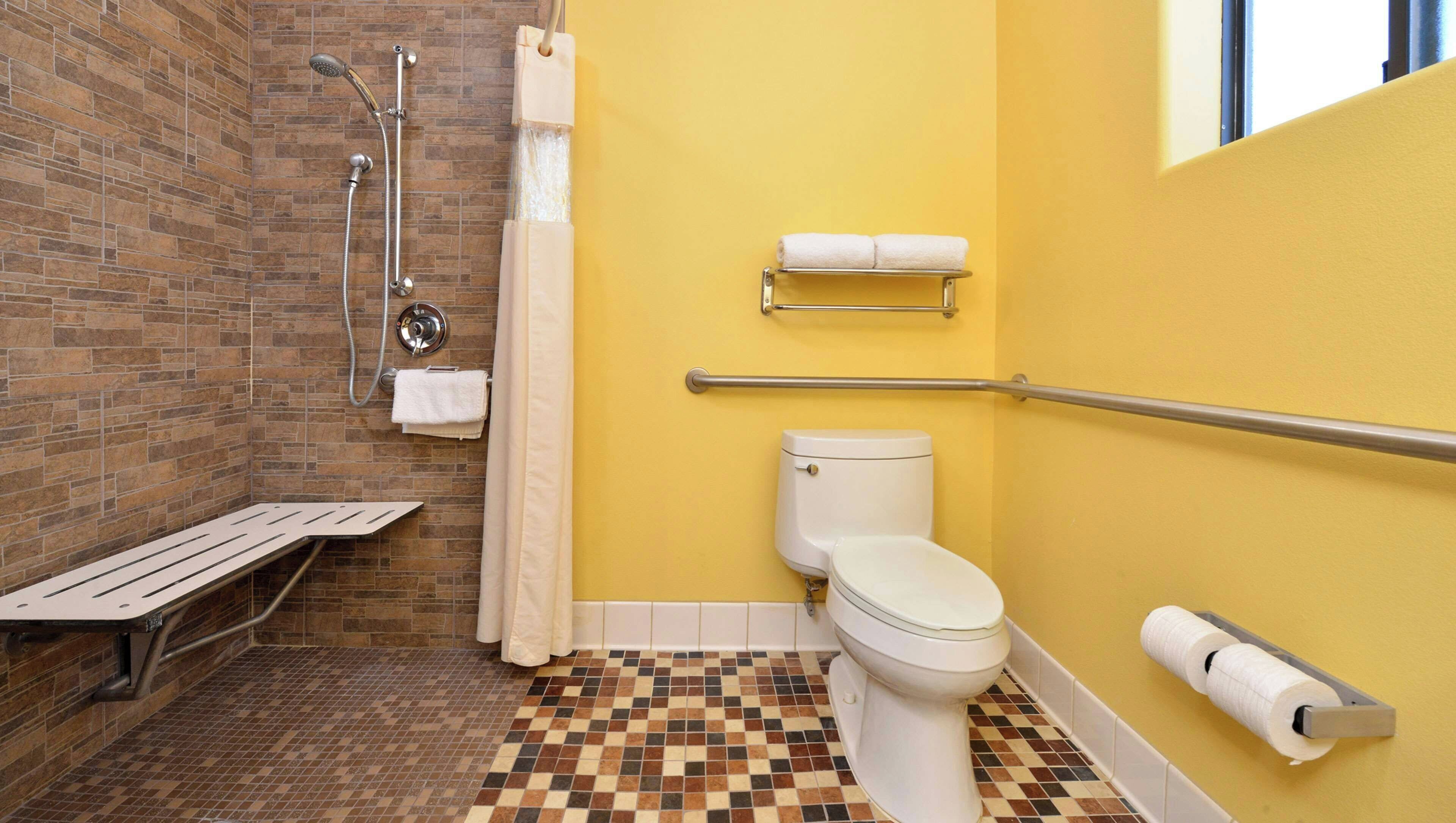 A bathroom with a shower, toilet, and bench, featuring a checkered floor and yellow walls.