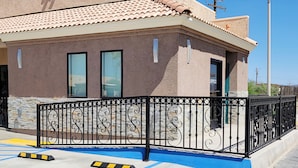 A building with a stone facade, a metal fence, and a blue painted area. - Magnuson Hotel Blythe (Blythe)