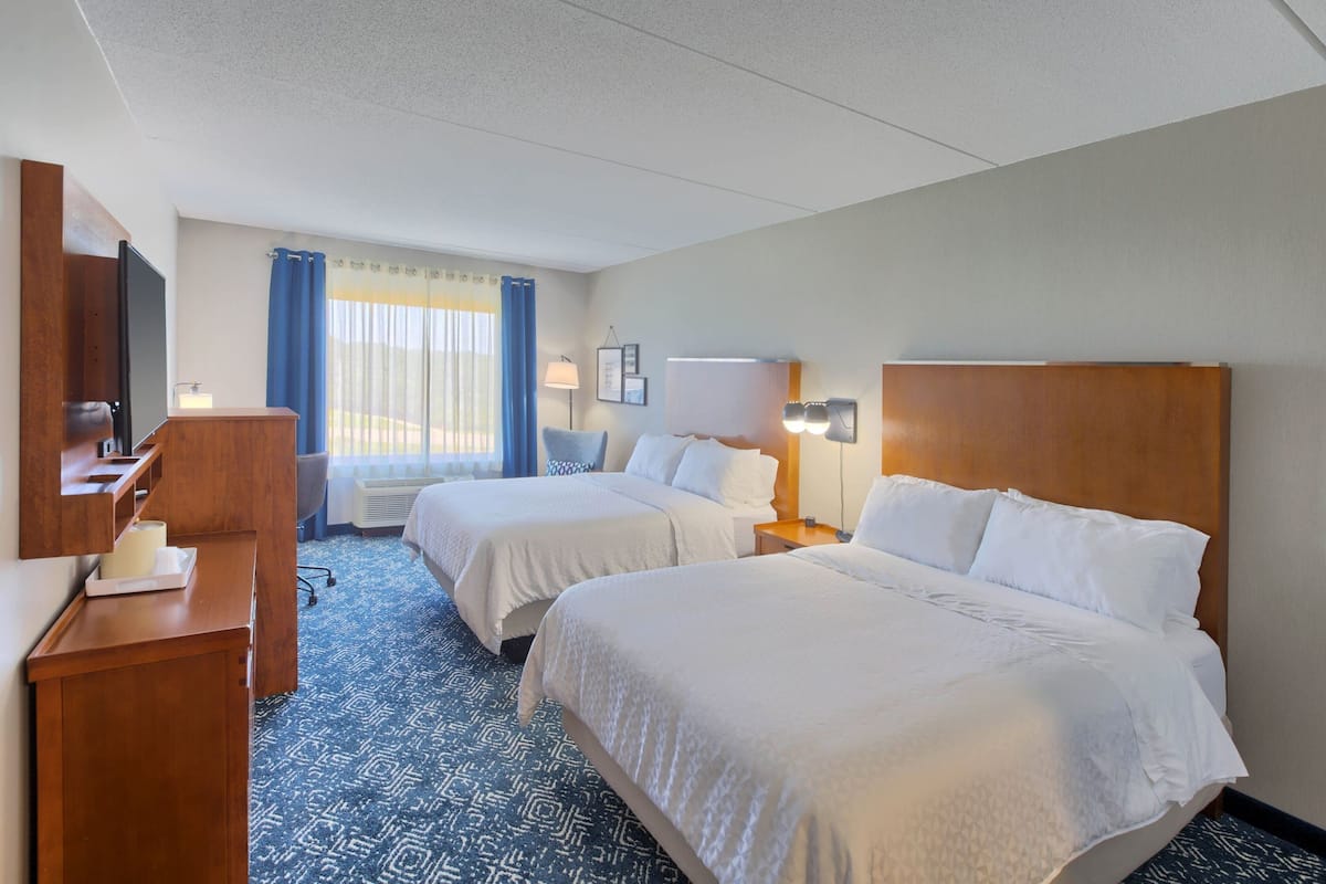 A hotel room with two beds, a desk, a TV, and a window with curtains.