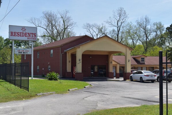 A building labeled "Residents Suites" with a covered entrance, a Coca-Cola vending machine, and a parking lot with cars.
