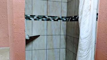 Ein kleiner, abgeschlossener Duschbereich mit einer gefliesten Wand, einer Duschbrause und einem weißen Duschvorhang.