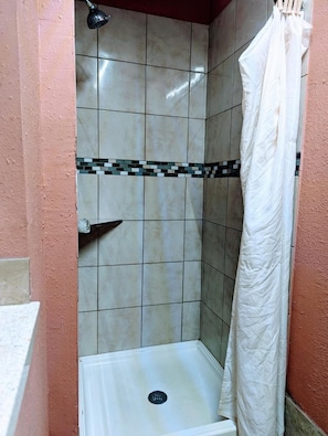 A small, enclosed shower area with a tiled wall, a showerhead, and a white shower curtain.