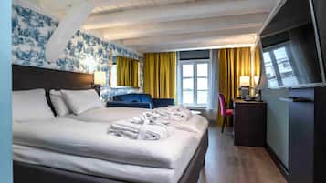 A hotel room with a large bed, a desk, a chair, a TV, and a window with curtains.