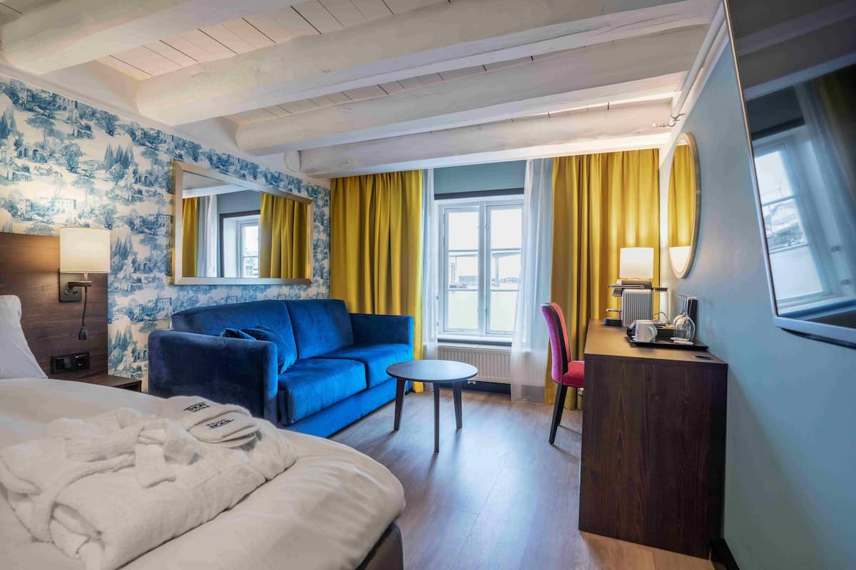 Une chambre d’hôtel avec un lit, un canapé bleu, une petite table ronde, un bureau avec une chaise et un grand miroir.