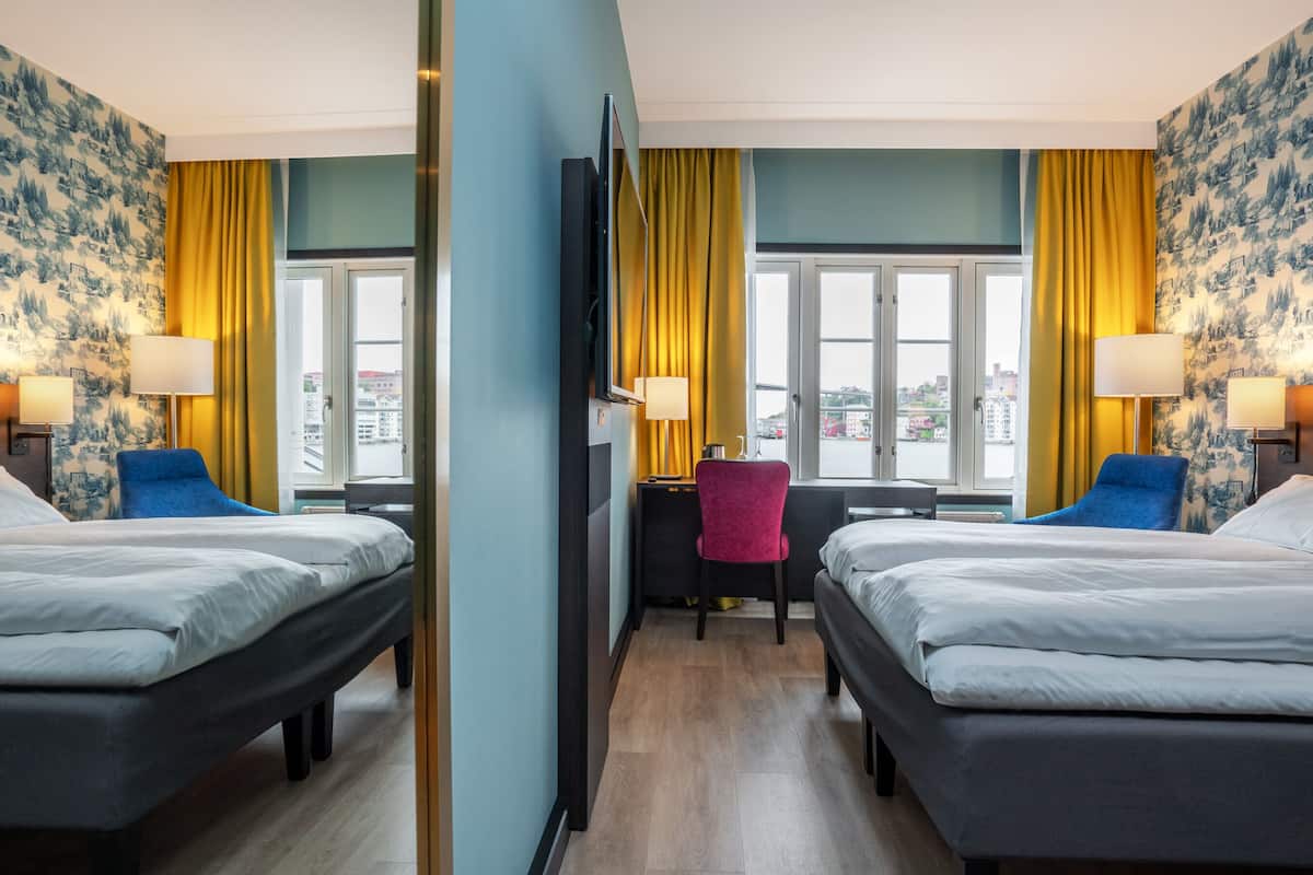 Une chambre d’hôtel avec deux lits, un bureau, une chaise et une télévision.
