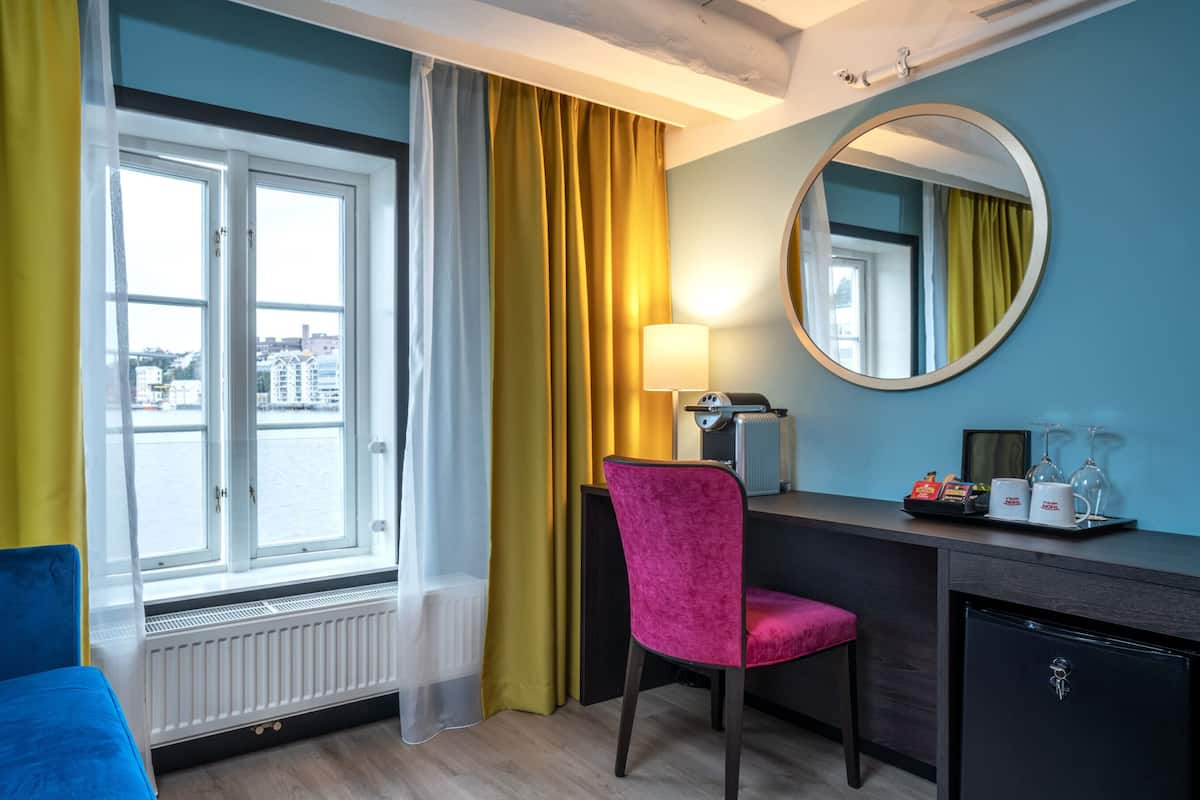 Une chambre d’hôtel comprenant un lit, un bureau avec une chaise, un miroir, une fenêtre avec des rideaux et un radiateur.