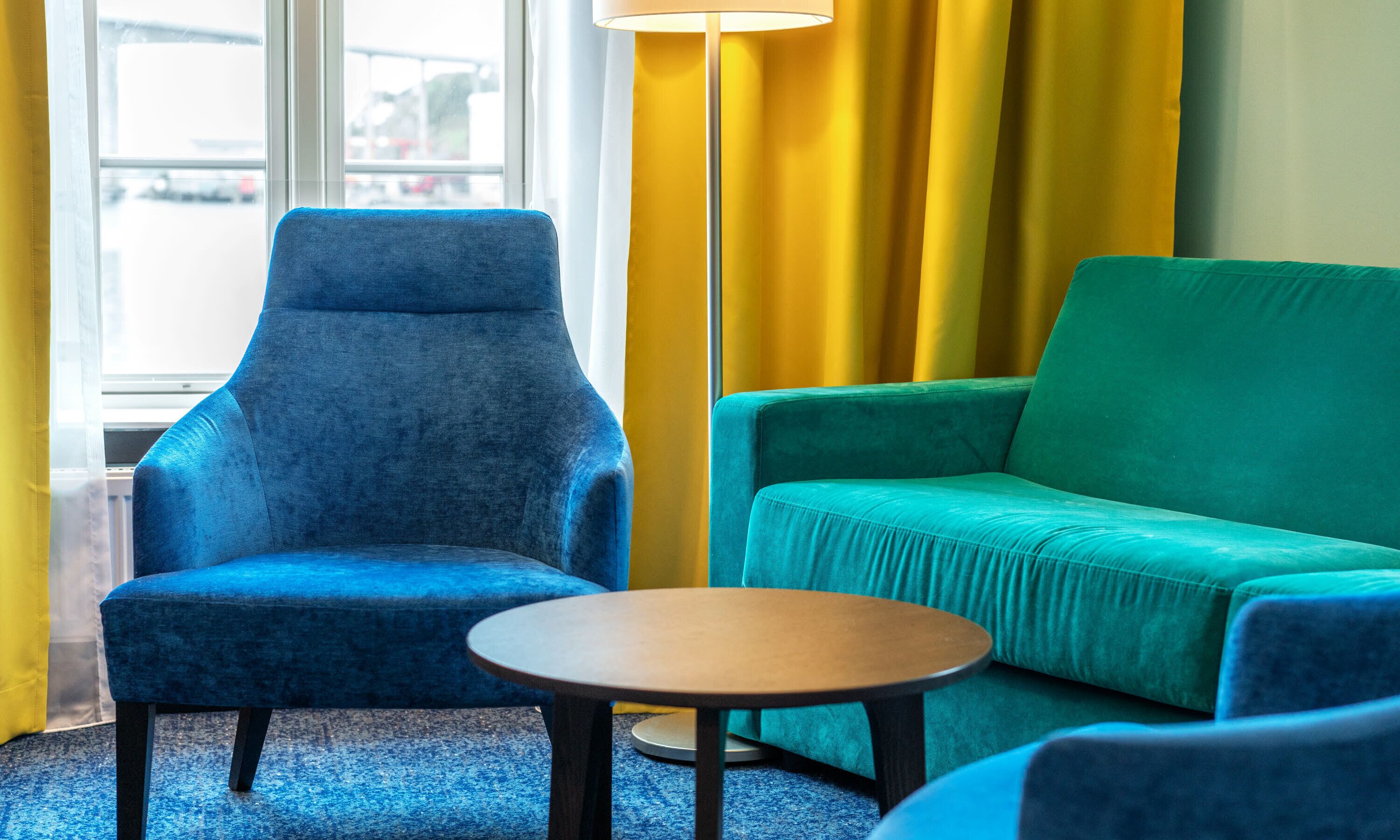 Um quarto com uma poltrona azul, um sofá verde e uma mesa redonda pequena.
