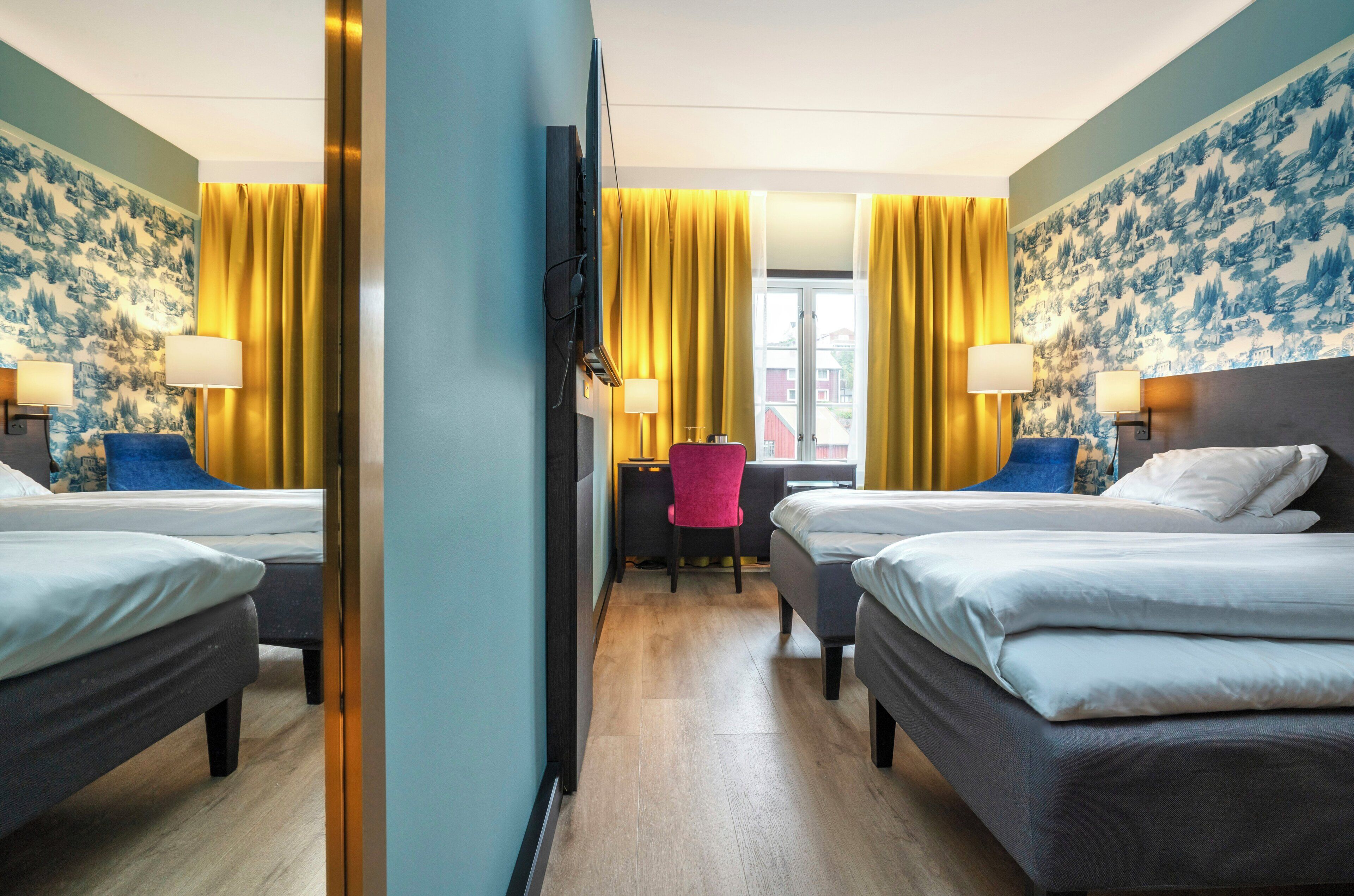 A hotel room with two beds, a desk, and a chair.