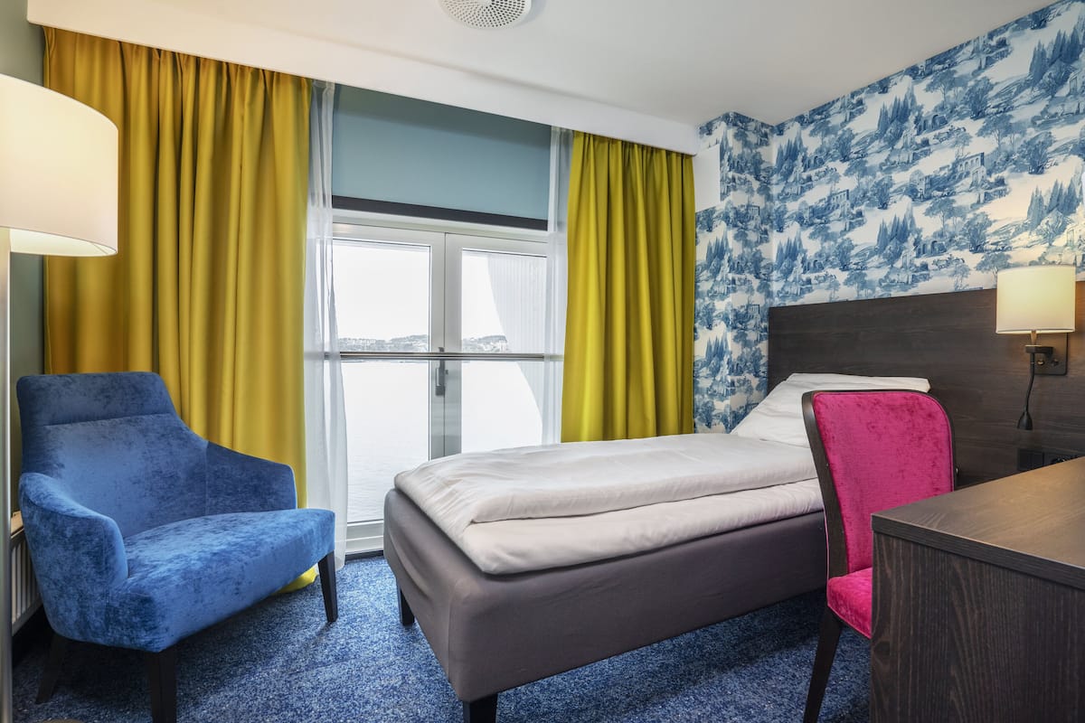 Une chambre d’hôtel avec un lit, un fauteuil bleu, une chaise rose et un bureau en bois.
