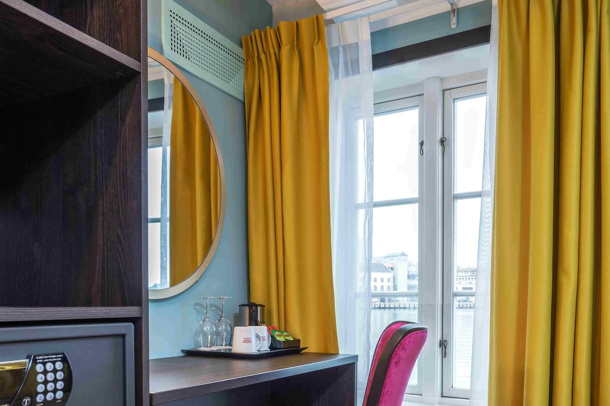 Une chambre d’hôtel équipée d’un bureau, d’une chaise, d’un coffre-fort, d’un miroir et d’une fenêtre avec des rideaux.