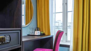 Une chambre d’hôtel équipée d’un bureau, d’une chaise, d’un coffre-fort, d’un miroir et d’une fenêtre avec des rideaux.