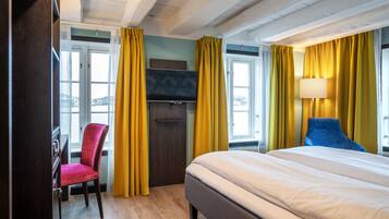 A hotel room with a bed, a TV, a desk, a chair, and yellow curtains.