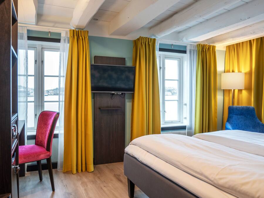 A hotel room with a bed, a TV, a desk, a chair, and yellow curtains.