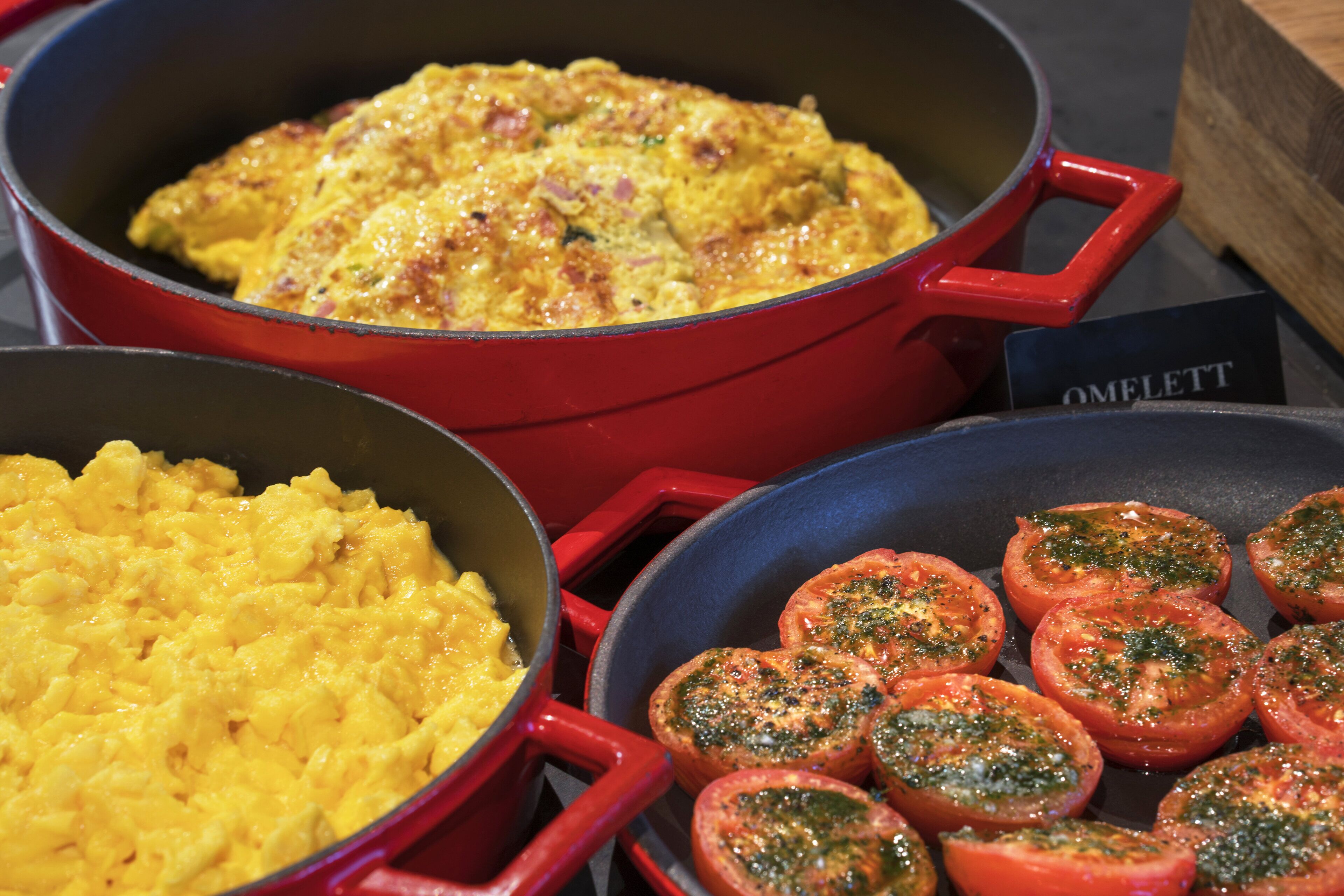 Een keuken met een rode pan met roerei en een pan met plakjes tomaat.