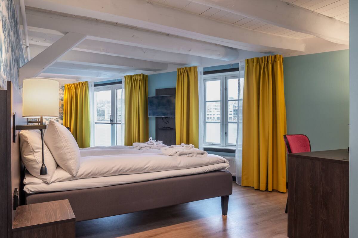 Ein Hotelzimmer mit Bett, Fernseher, Schreibtisch und einem Fenster mit Vorhängen.