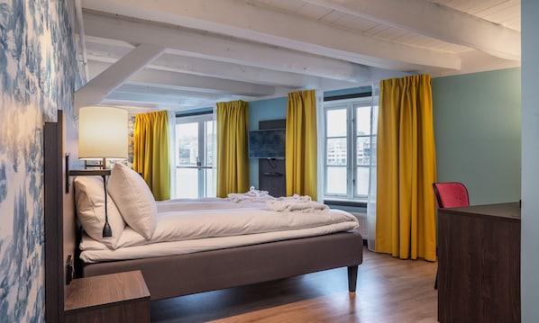 Una habitación de hotel con cama, televisión, escritorio y ventana con cortinas.