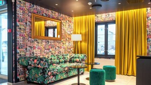 A hotel lobby with a colorful patterned wall, a sofa, two round tables, and yellow curtains. - Thon Hotel Kristiansund (Kristiansund)