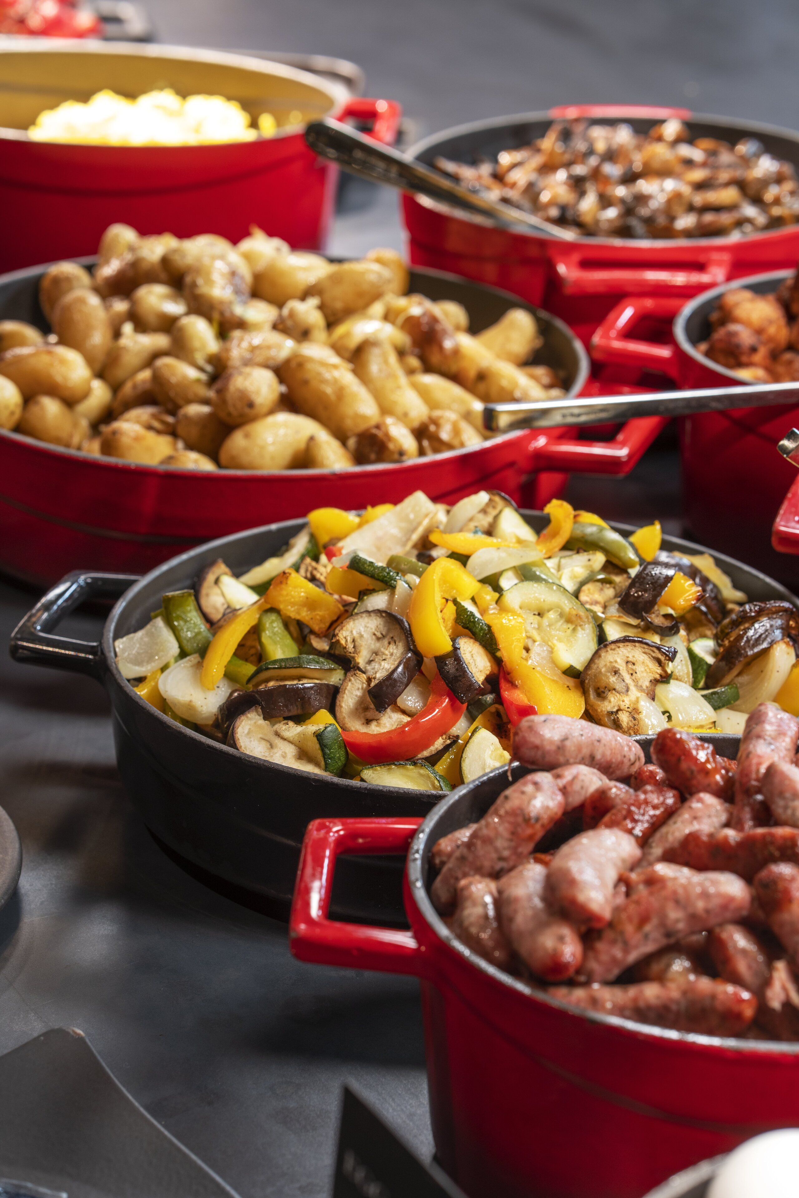 A buffet with various dishes including roasted potatoes, grilled vegetables, and sausages.