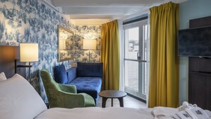 A hotel room with a bed, a green armchair, a blue sofa, a small round table, a TV, and a window with yellow curtains. - Thon Hotel Kristiansund (Kristiansund)