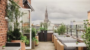 A rooftop patio with wicker furniture, potted plants, and a view of a church tower. - Home Hotel Folketeateret (Oslo)