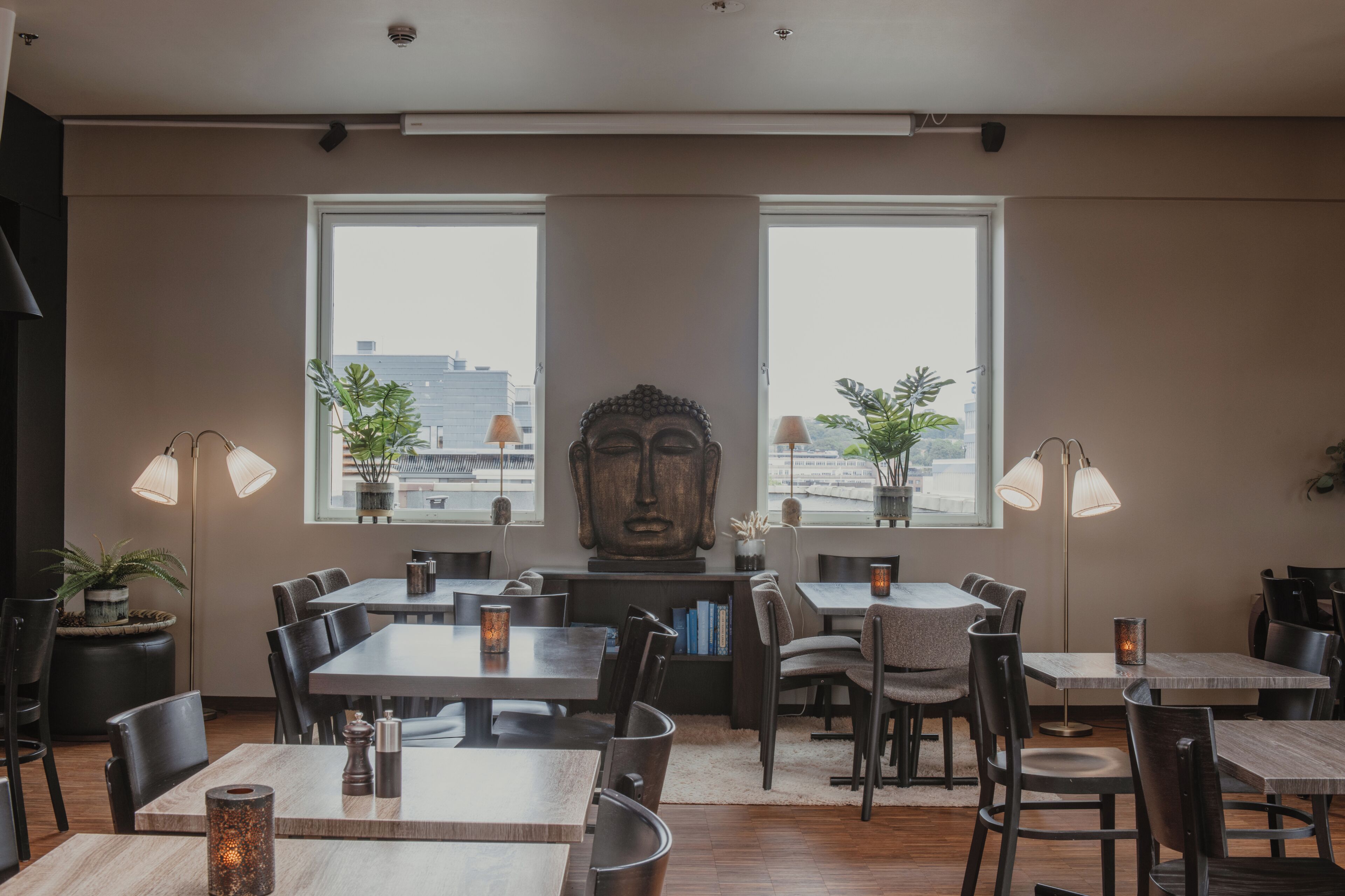 Un restaurante con mesas y sillas, amplias ventanas y una estatua de Buda.