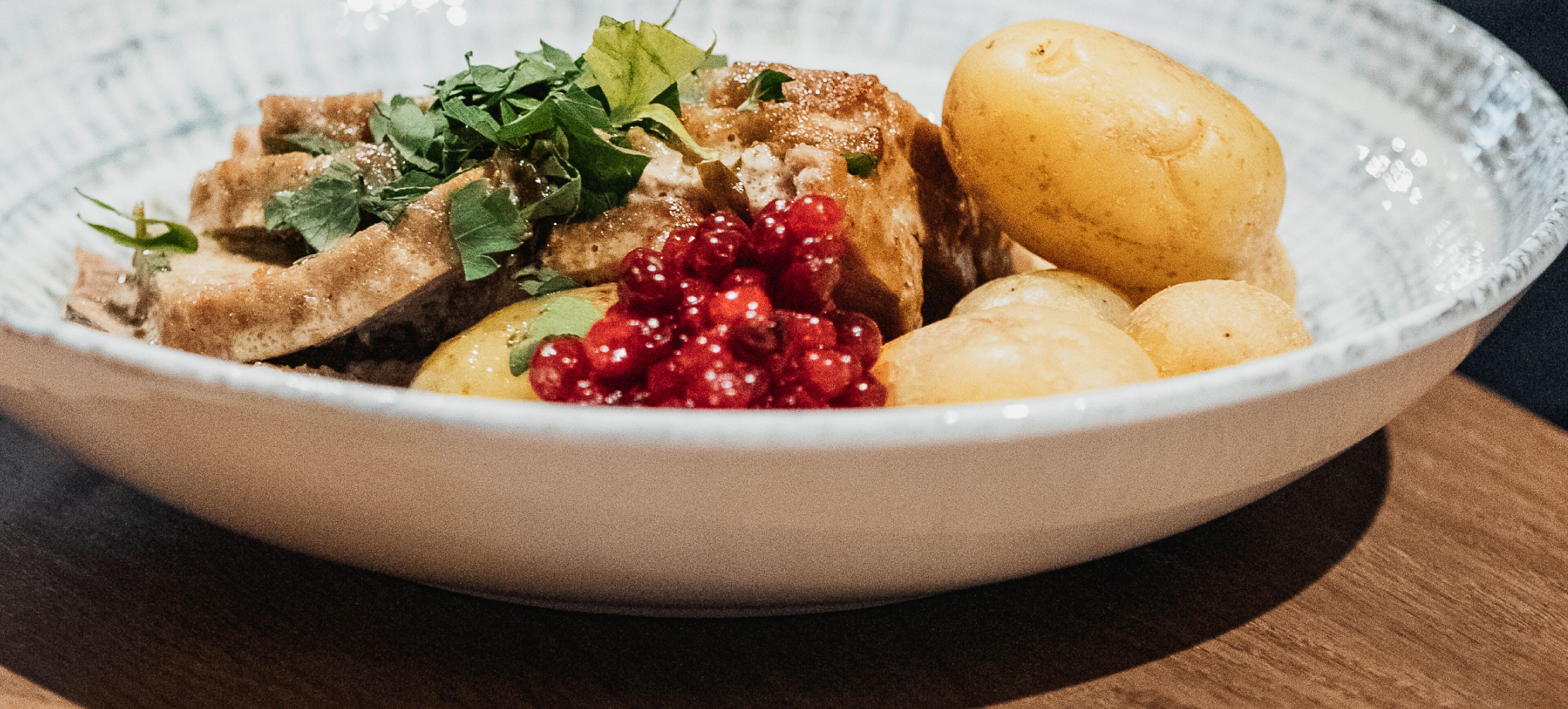 A bowl of food with meat, potatoes, and red berries.