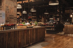 A bar area with wooden counters, hanging pendant lights, and shelves stocked with bottles. - Home Hotel Folketeateret (Oslo)