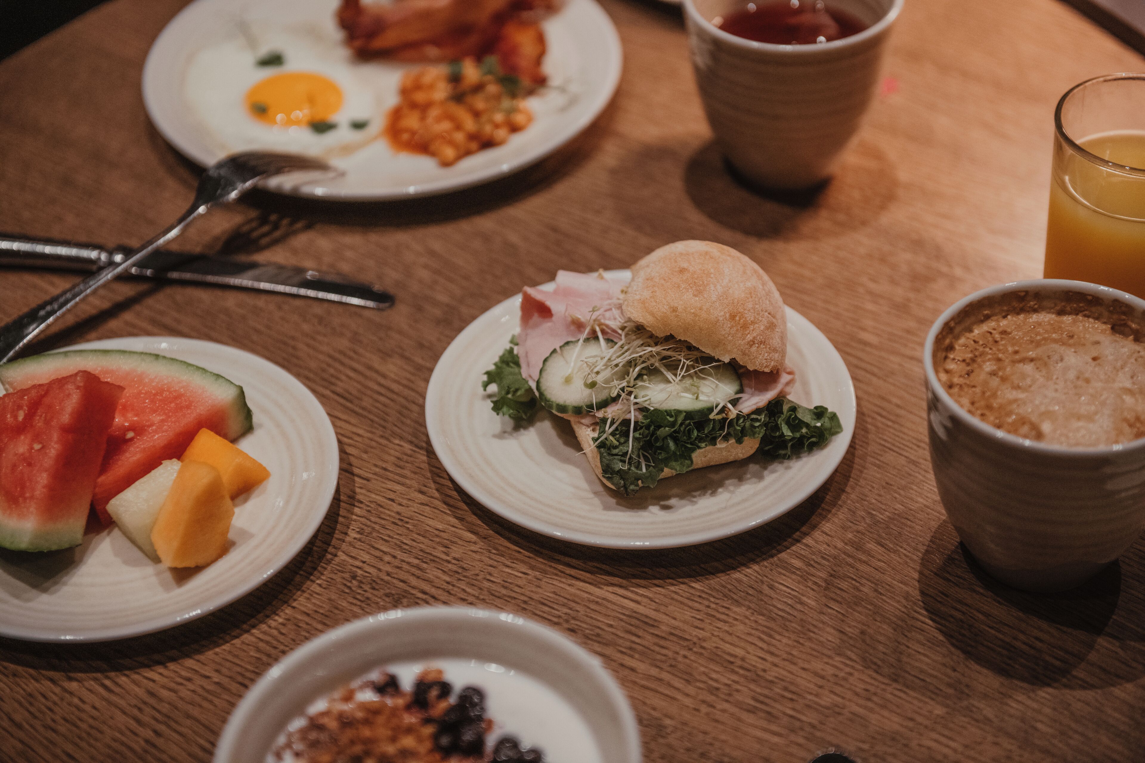 A breakfast setting with plates of food, a glass of orange juice, and a bowl of cereal.