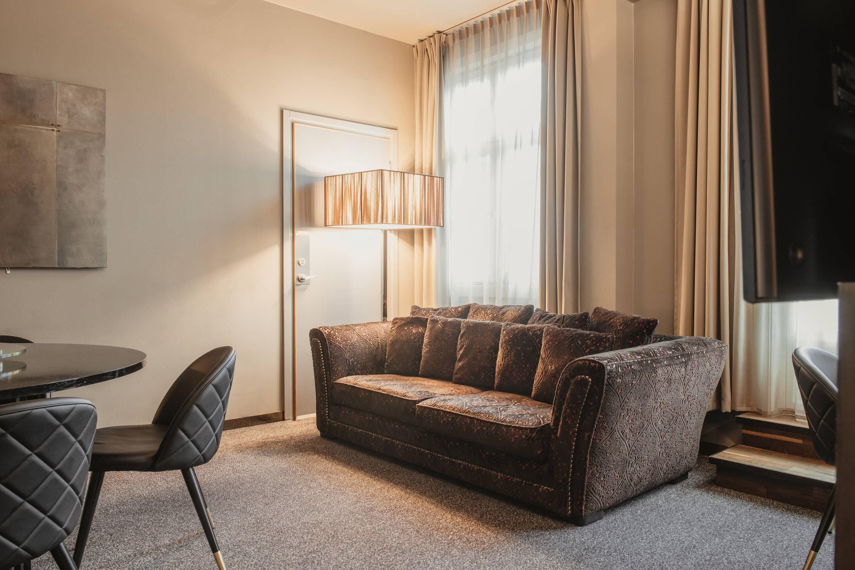 A room with a sofa, chairs, a lamp, and a TV.
