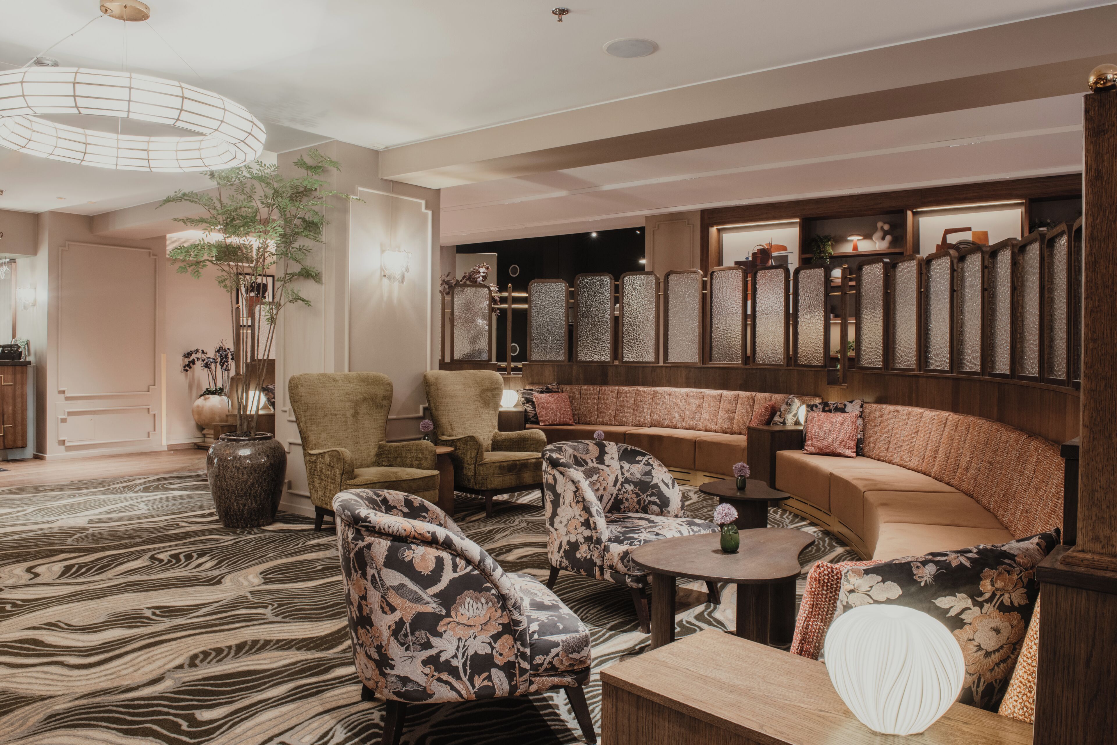A modern lounge area with a sofa, armchairs, a round table, and a decorative mirror.