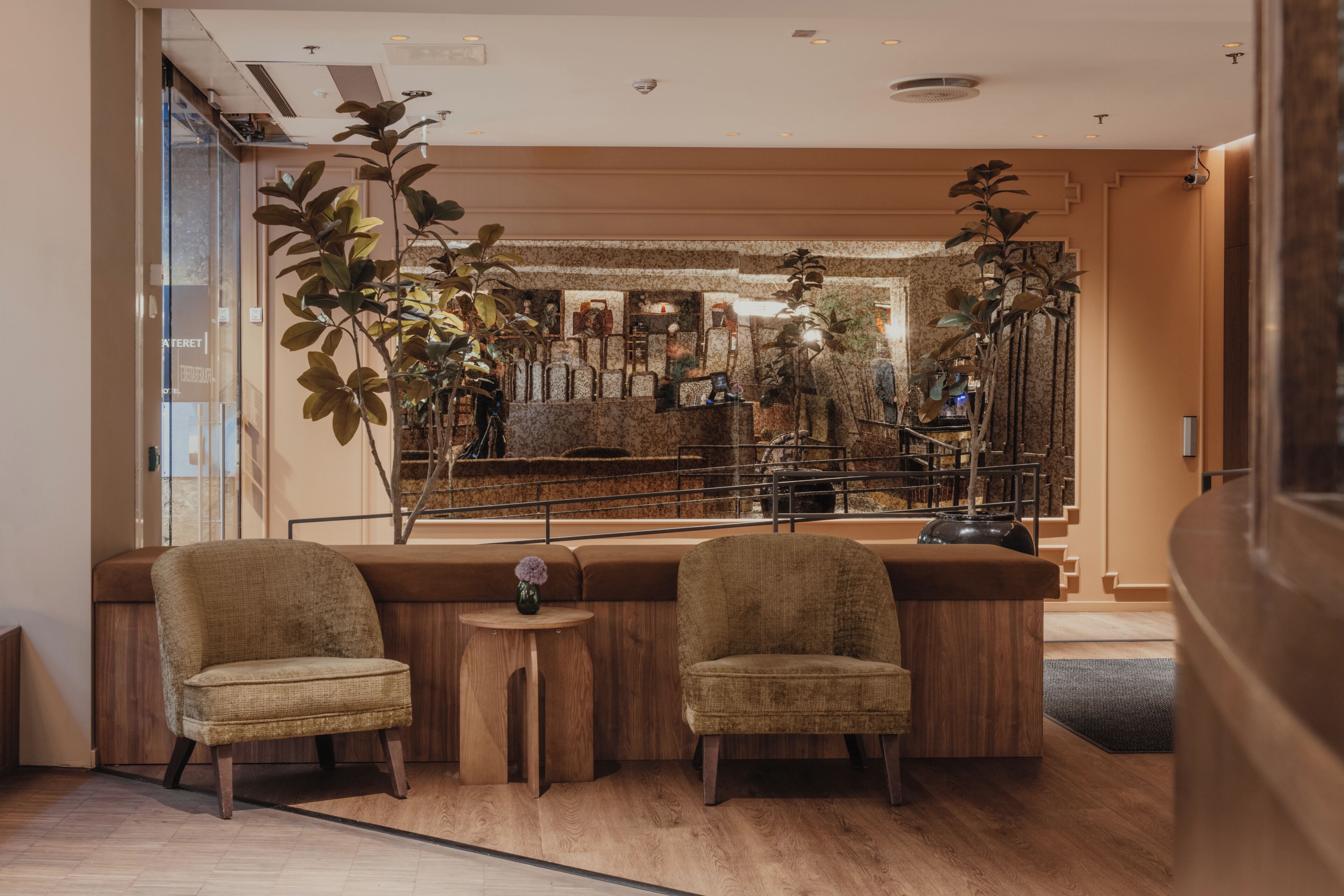 A modern bar area with two upholstered chairs, a small round table, and a large plant.