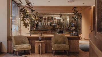 A modern bar area with two upholstered chairs, a small round table, and a large plant.