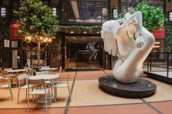 A modern indoor space with a sculpture, seating area, and a building entrance.