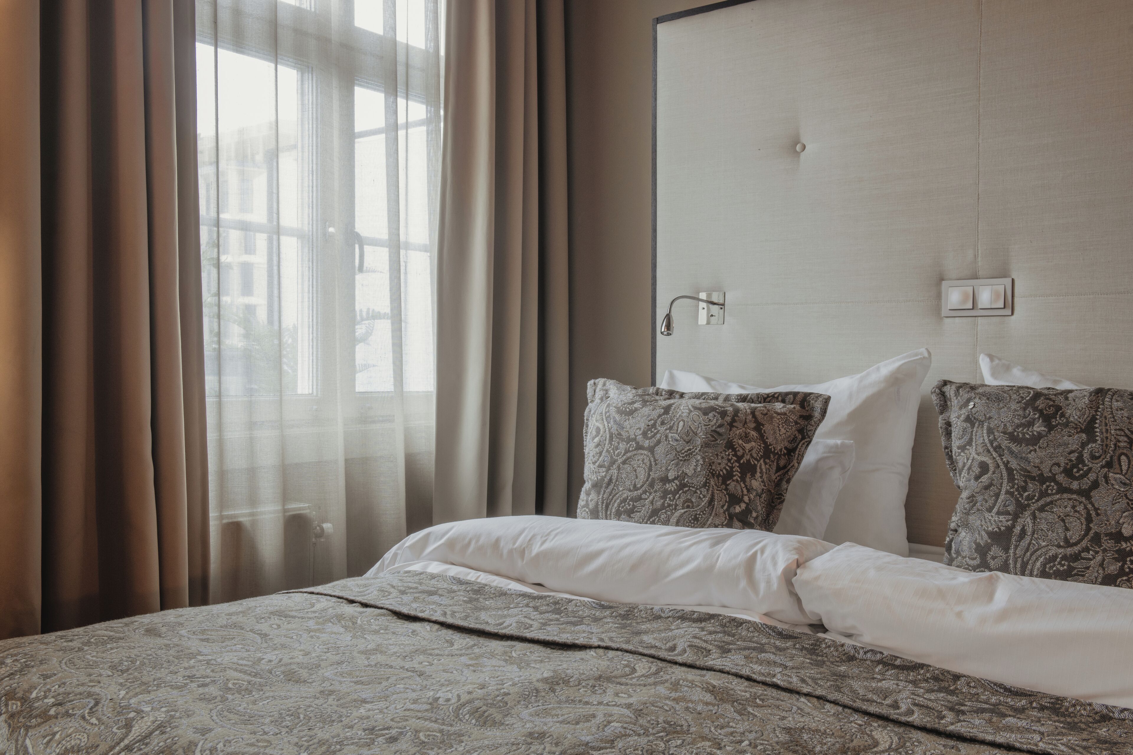 A hotel room with a bed, curtains, a headboard, and a window.