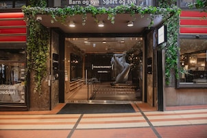 La entrada de un hotel con puerta de vidrio, un letrero que dice 'Folketeateret Home Hotel' y una gran escultura en el centro.